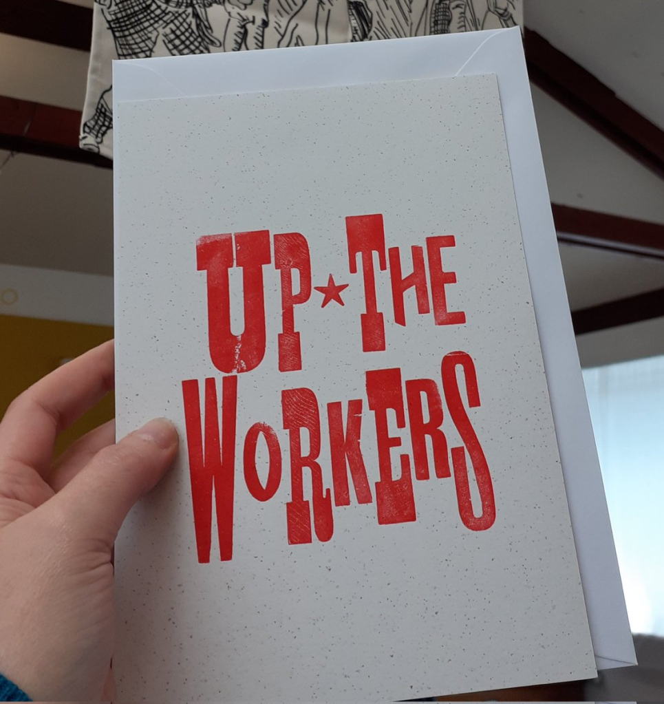 a hand holds a letterpress card with 'Up the Workers' printed on it